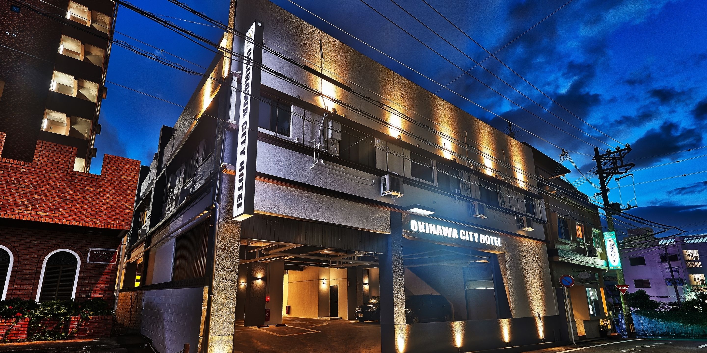 The exterior of Okinawa City Hotel with a modern design, multiple floors, and a parking garage entrance.