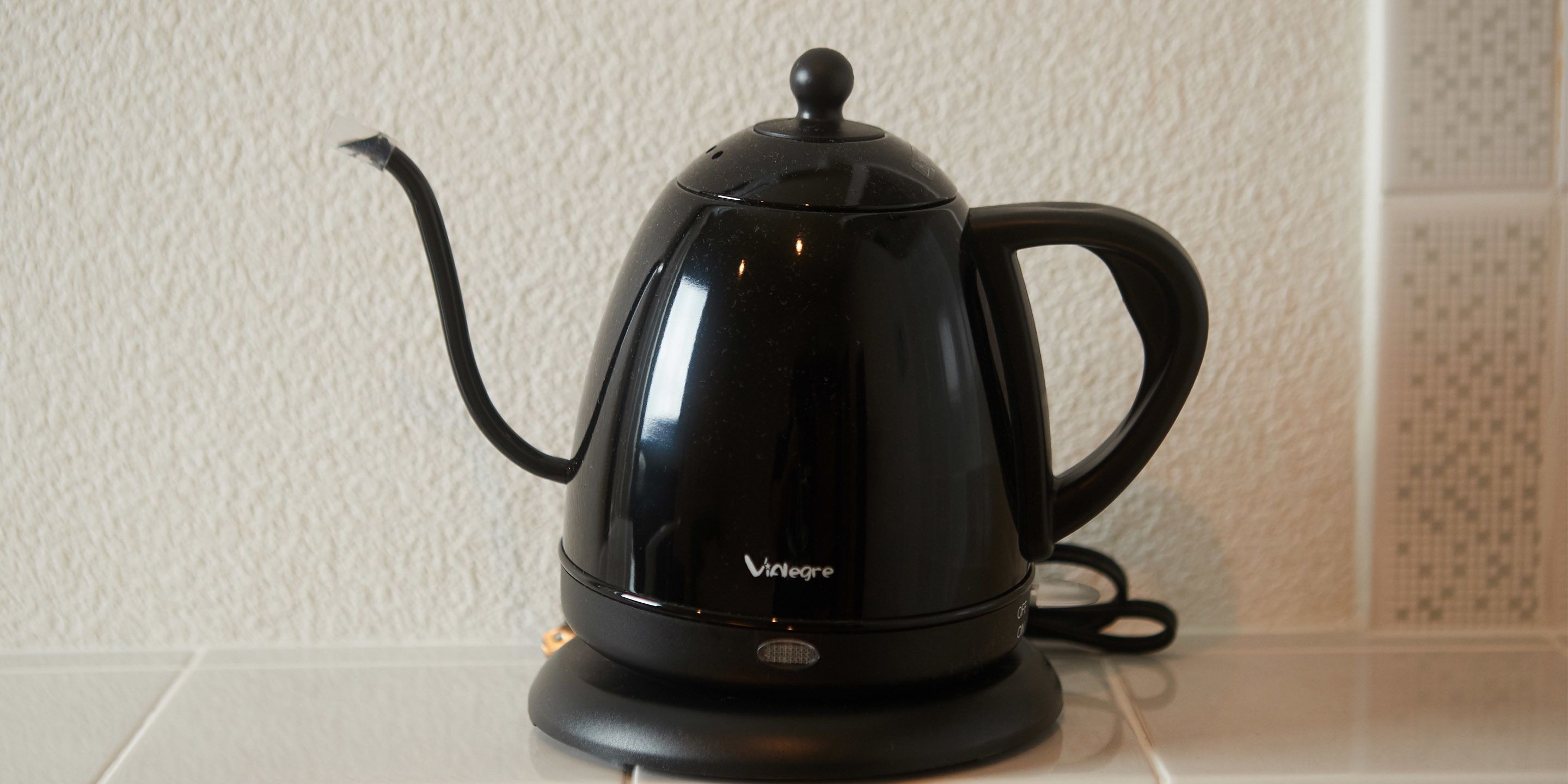 A black electric kettle with a lid and handle on a white countertop.