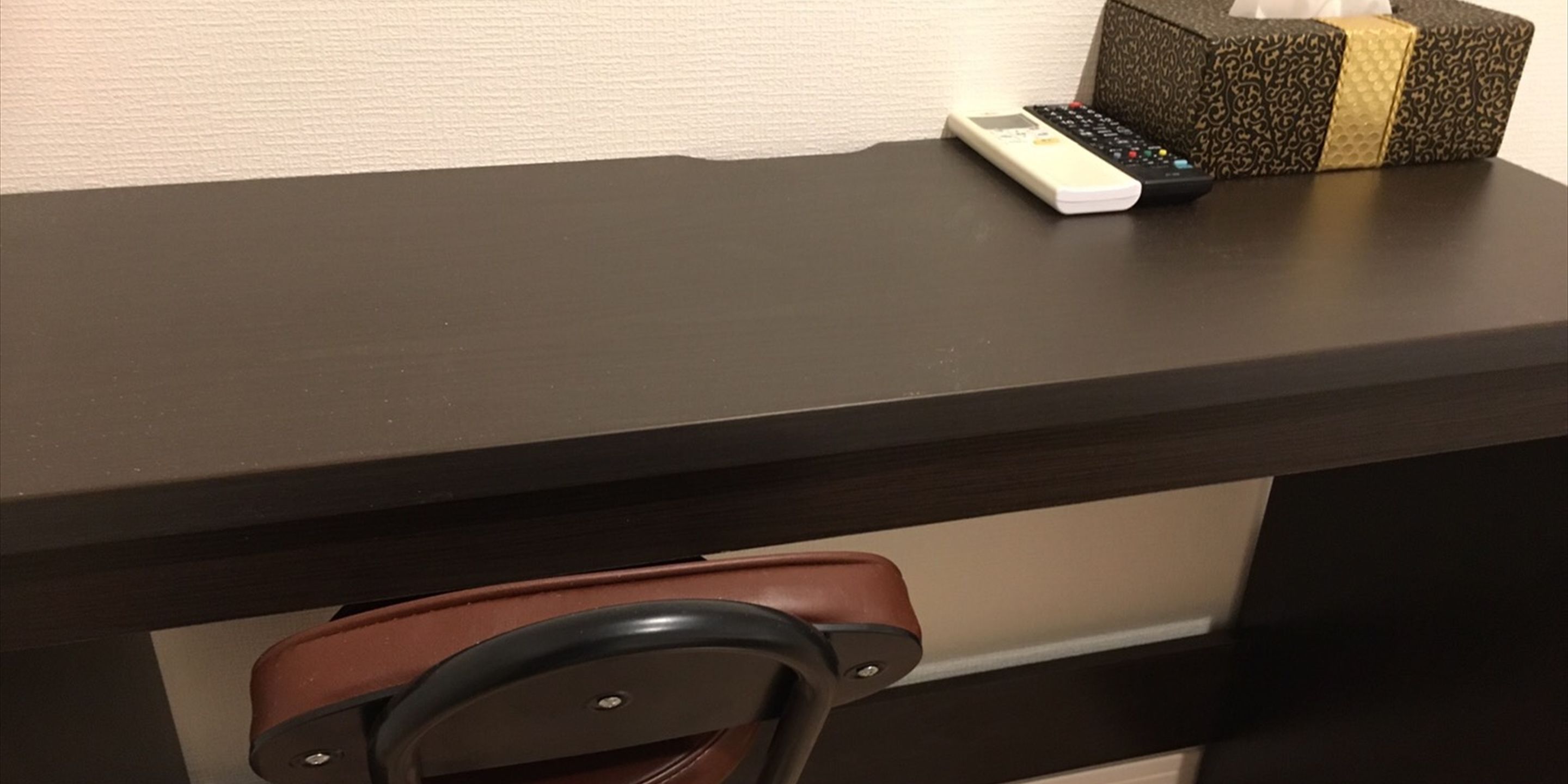 A dark wooden desk with a remote control and a decorative box on top.