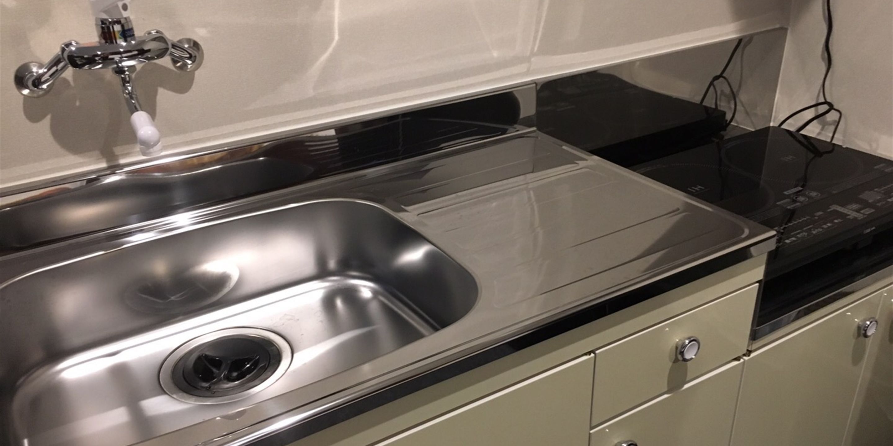 A stainless steel kitchen sink with a single faucet, a black countertop, and a beige cabinet below.