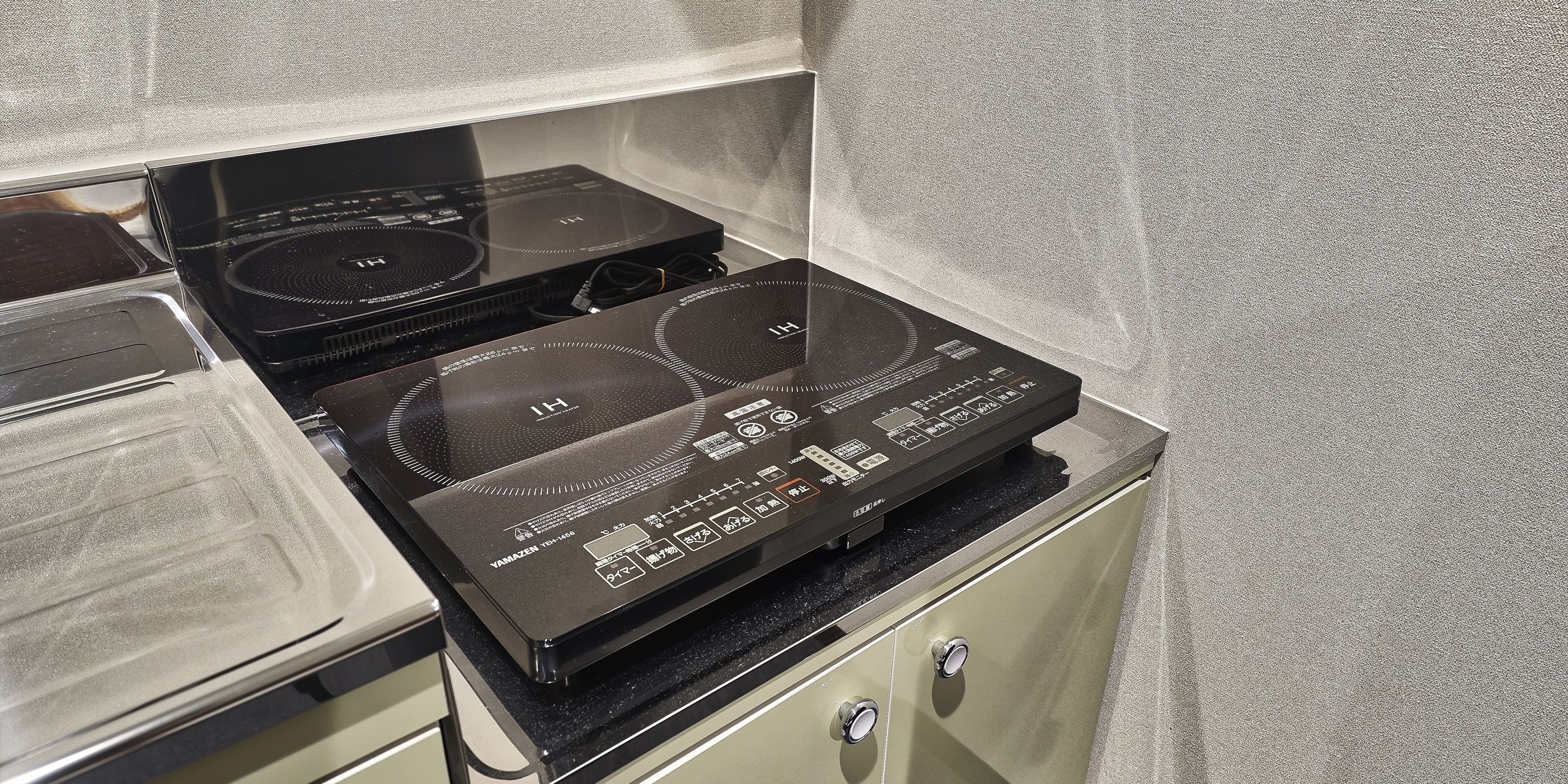 Una cocina con dos fogones de inducción negros y un horno de acero inoxidable.