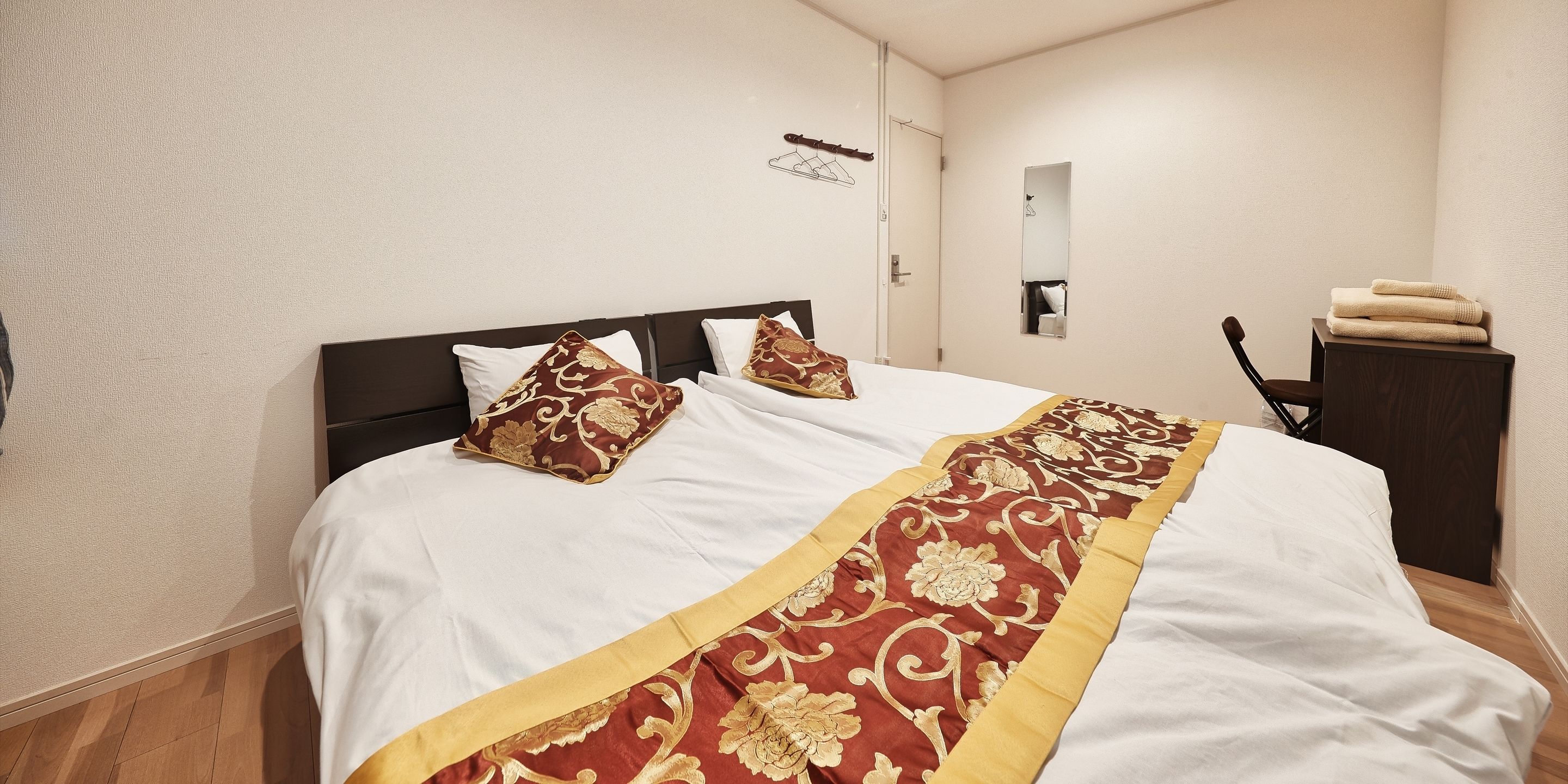 A neatly made bed with white and red bedding, a wooden headboard, and a small bedside table with a towel.