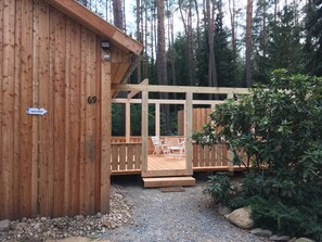 A wooden cabin with a deck and a sign indicating the number 69. - The holiday home "Ortheide 69" is located in a forest settlement with large trees. (Böddenstedt)