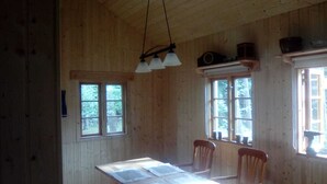 Une cabane en bois comprenant un coin repas, deux fenêtres et un luminaire suspendu.