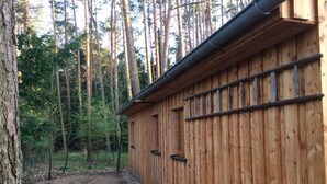 Une cabane en bois, accessible par un sentier de terre, entourée de grands arbres.