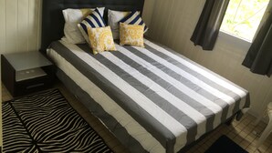 Ein Bett mit gestreifter Bettwäsche, zwei Kissen, ein Nachttisch und ein Zebra-Teppich.