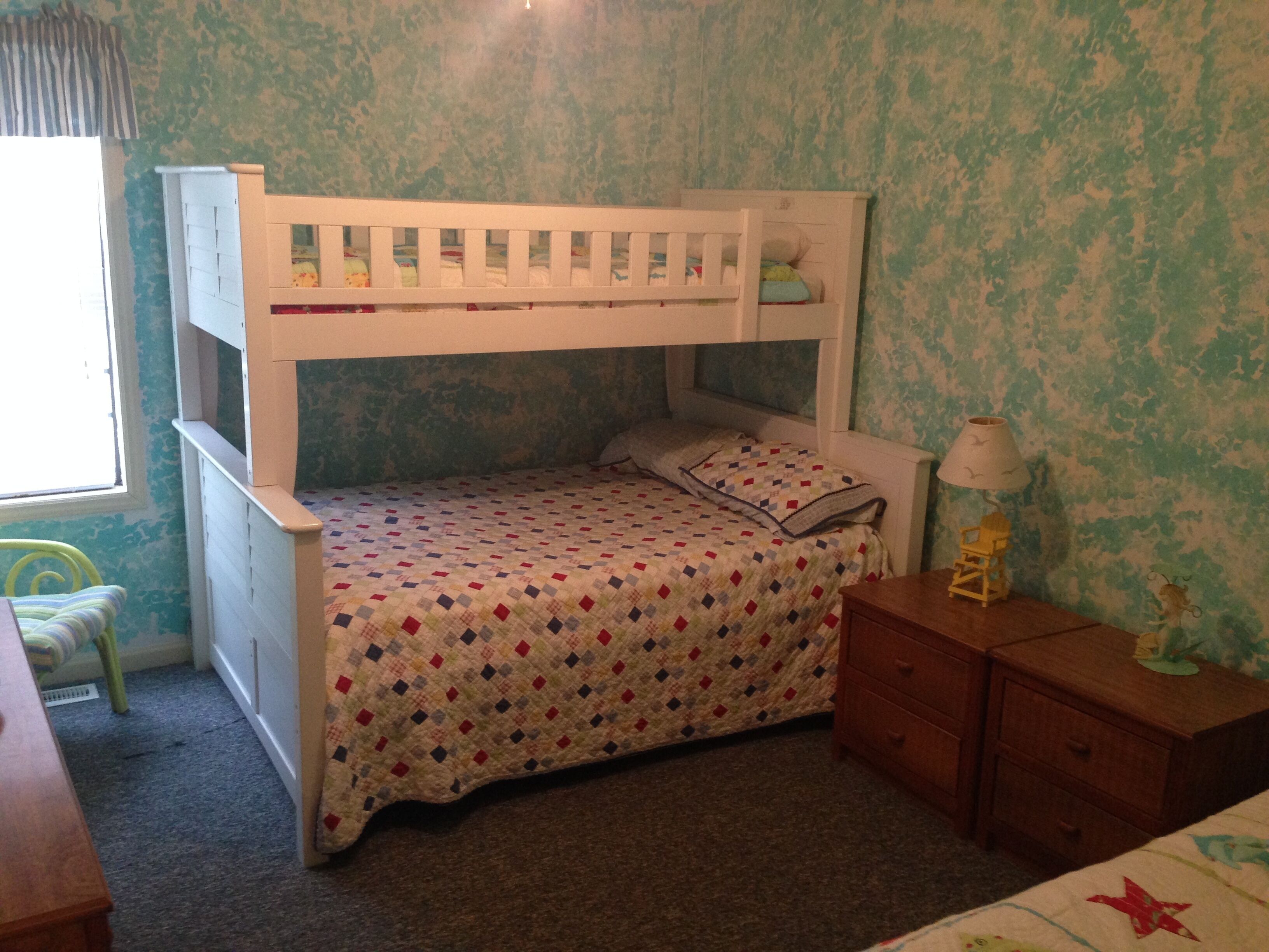 Ein Kinderstockbett mit einem gemusterten Bettbezug, ein Nachttisch, eine Lampe und ein kleiner Stuhl.