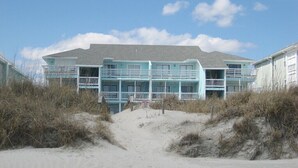 Ein Hotel direkt am Strand mit mehreren Balkonen, einem Sandstrand davor und blauem Himmel.
