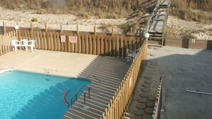 Ein Poolbereich mit Holzterrasse, Sandstrand und Holzlattenzaun.