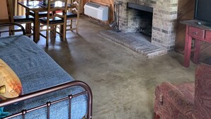 A rustic interior with a stone fireplace, wooden beams, a dining area, and a television. - The Sundance Cabin at the Hideaway Ranch and Refuge (Bluff Dale)