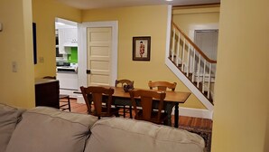 Una sala de estar con sofá, mesa de comedor, sillas y una escalera que lleva a una cocina.