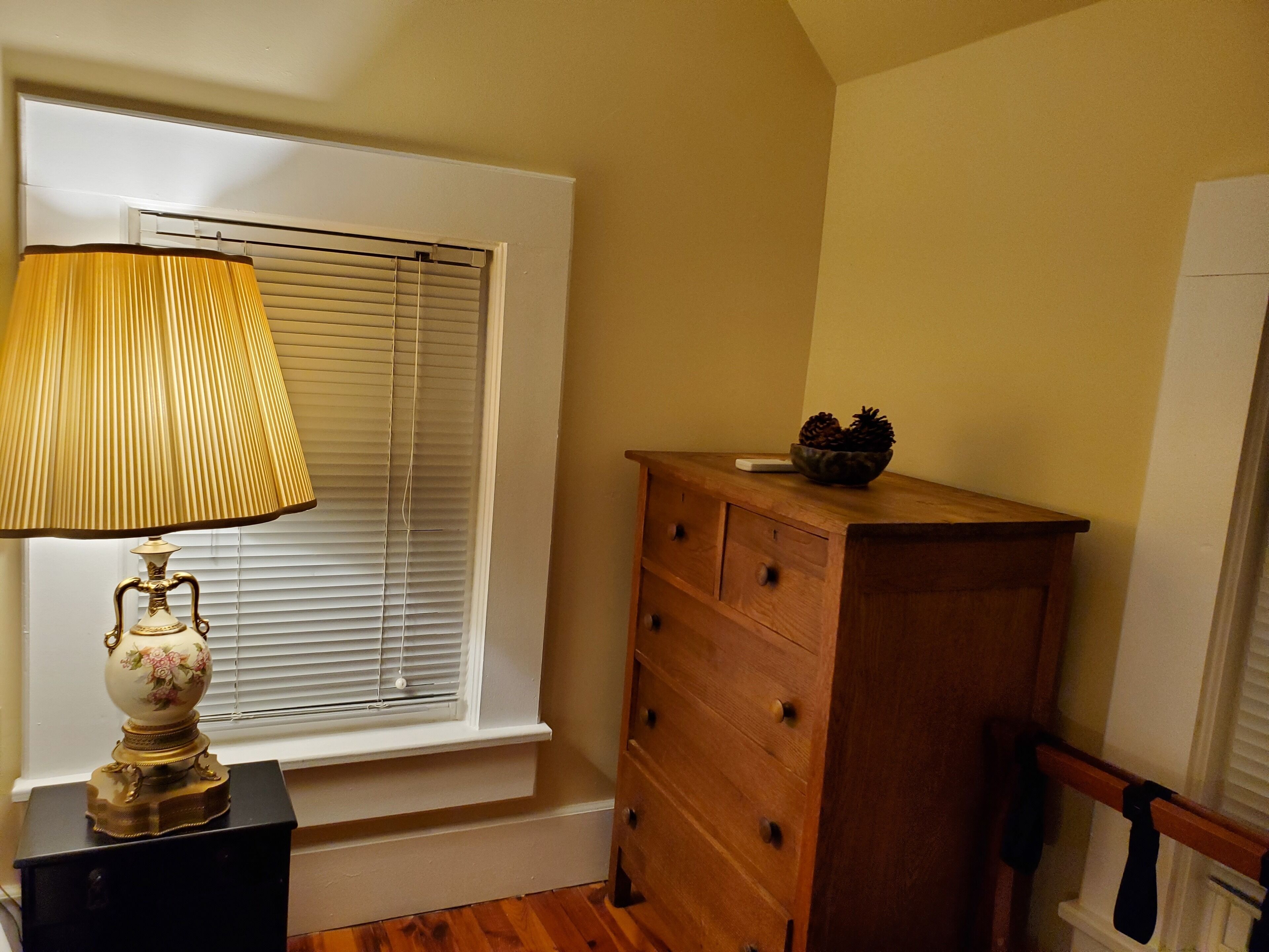 Una habitación con ventana, un aparador de madera y una lámpara sobre una mesa.