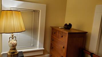 Una habitación con ventana, un aparador de madera y una lámpara sobre una mesa.