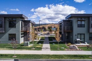 Um complexo de apartamentos moderno com edifícios de dois andares, um caminho central e montanhas ao fundo.
