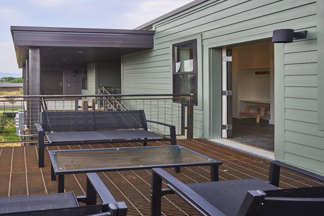 A covered outdoor seating area with metal tables and chairs, a staircase leading to an upper level, and a door leading to an interior space.