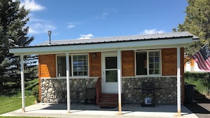 Une petite cabane aux murs en pierre, une véranda avec deux chaises et un drapeau américain.