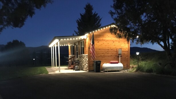 Une cabane en bois dotée d’un porche couvert, d’un barbecue et d’un petit abri de jardin.