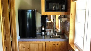 Une cuisine de taille réduite, dotée de meubles en bois, d’un réfrigérateur noir, d’un four à micro-ondes et d’un évier.