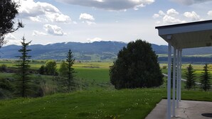Un espace extérieur abrité offrant une vue sur un champ verdoyant et des montagnes lointaines.