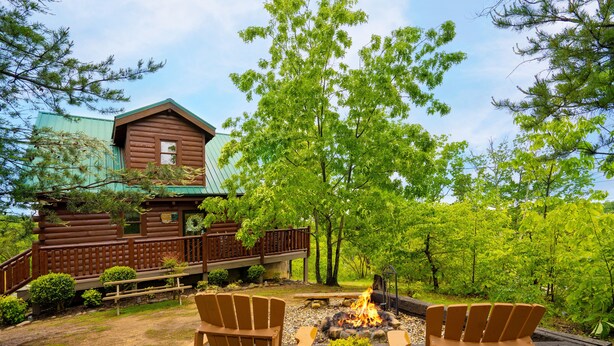 A cabin with a deck, two Adirondack chairs, a fire pit, and a view of the surrounding forest. - Enchanted Hideaway: Honeymoon, S/Secluded, Fire Pit, Hot Tub, Top Amenities, near Attractions! (Sevierville)