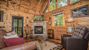 A wooden cabin interior with a fireplace, leather furniture, and a stone fireplace surround. - Enchanted Hideaway: Honeymoon, S/Secluded, Fire Pit, Hot Tub, Top Amenities, near Attractions! (Sevierville)