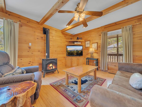 A cozy cabin interior with a wooden interior, a fireplace, a ceiling fan, and a television.