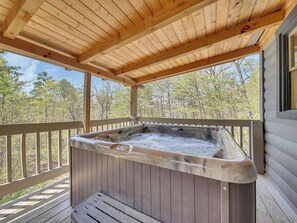 Una terraza de madera con un jacuzzi bajo una pérgola de madera, rodeada de árboles.