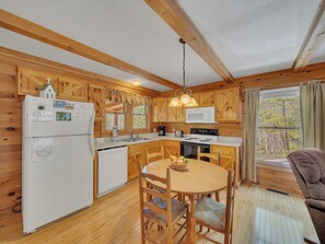 A wooden cabin kitchen with a refrigerator, microwave, stove, and dining table with chairs.