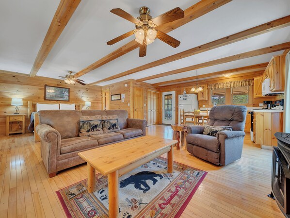A spacious living room with a wooden ceiling, a sofa, a chair, a coffee table, and a dining area.
