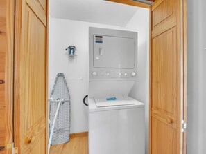 A laundry room with a front-loading washing machine, a drying rack, and wooden cabinets.