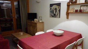 Un coin repas avec une table recouverte d’une nappe rouge, des chaises blanches et un bol blanc posé sur la table.