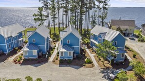 A cluster of blue houses with a waterfront view, arranged in a row with a paved driveway and a small garden area in front. - Neuse Village #7 - Experience your inner peace! (Arapahoe)