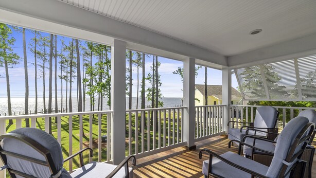 A covered outdoor seating area with white railings and wicker chairs, overlooking a grassy area and a body of water. - Neuse Village #7 - Experience your inner peace! (Arapahoe)