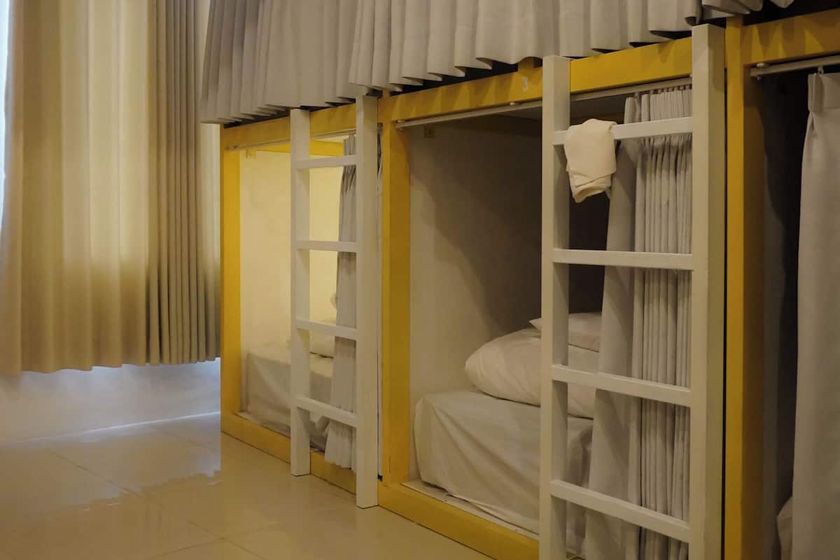 A hotel room with bunk beds, curtains, and a tiled floor.
