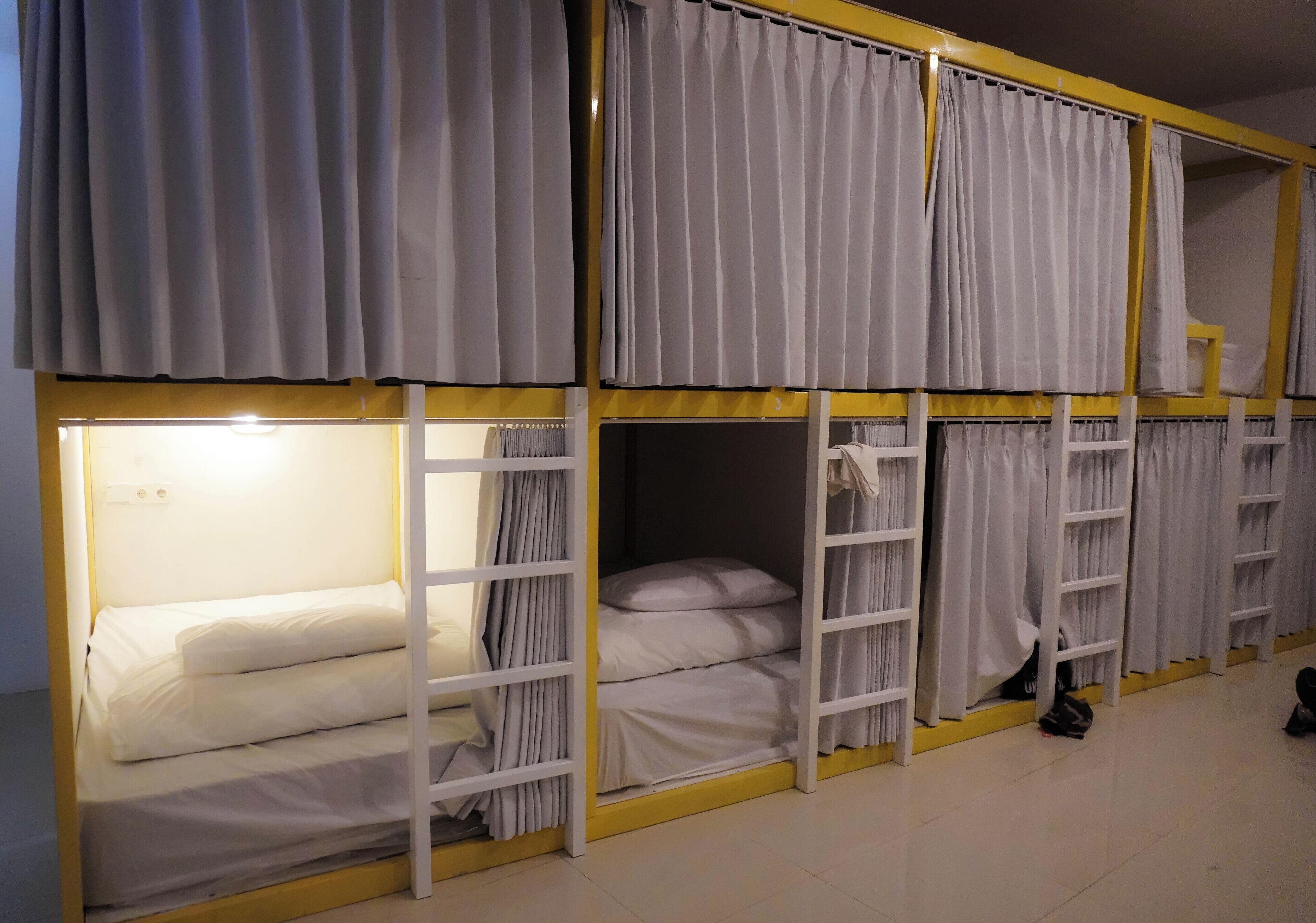 A dormitory-style room with bunk beds, curtains, and a shelf with personal items.