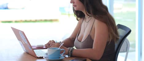 A person sitting at a table with a laptop, a cup, and a smartphone.