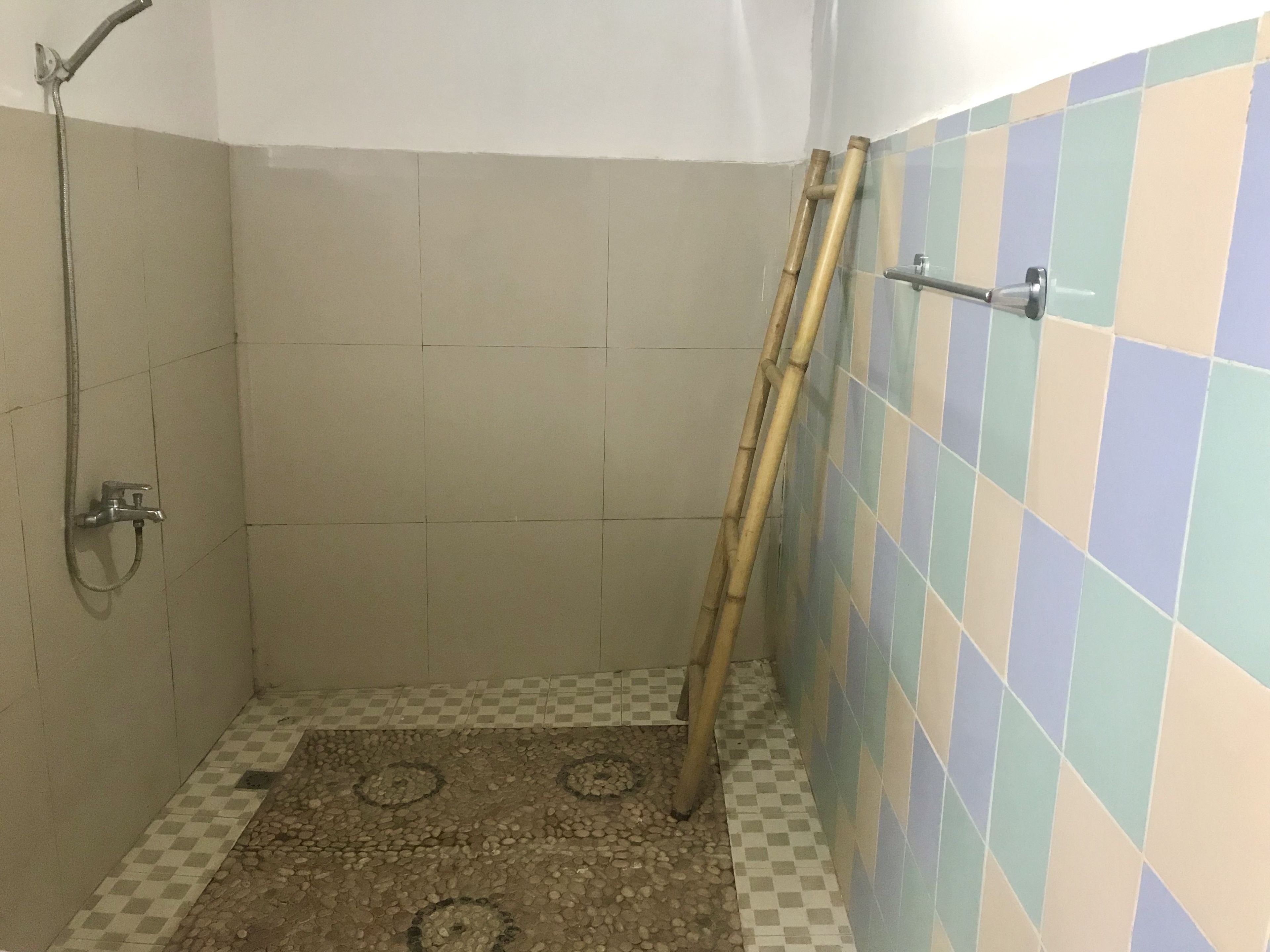 Un área de ducha con suelo a cuadros, una escalera de bambú y un cabezal de ducha.