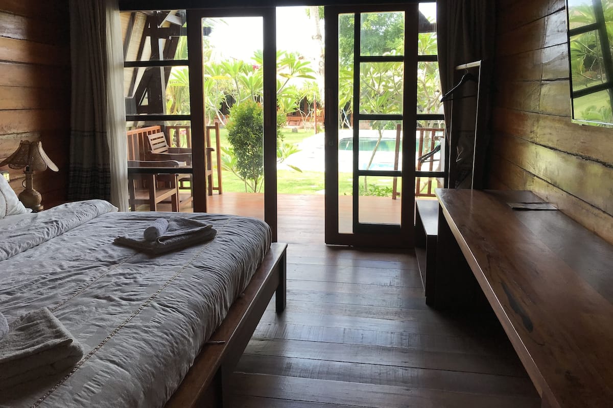A wooden room with a bed, a desk, and a view of a garden and pool.