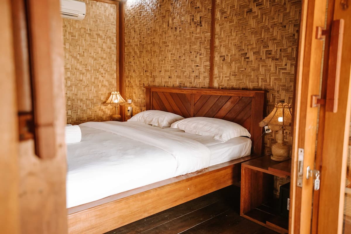 A room with a bed, a nightstand, a lamp, and a woven wall.
