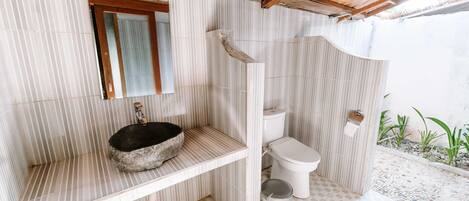 Une salle de bain avec un lavabo en pierre, des toilettes et un espace douche.