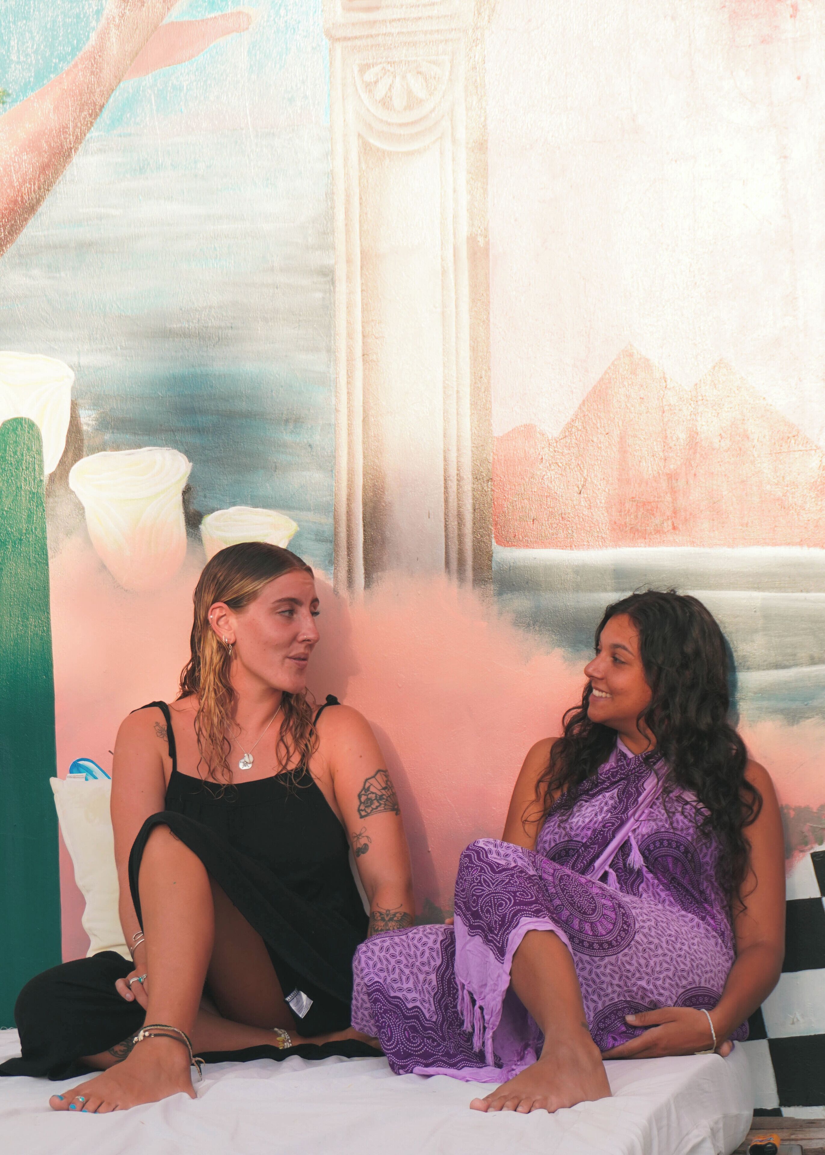 Dos personas sentadas en una cama con un mural de fondo.
