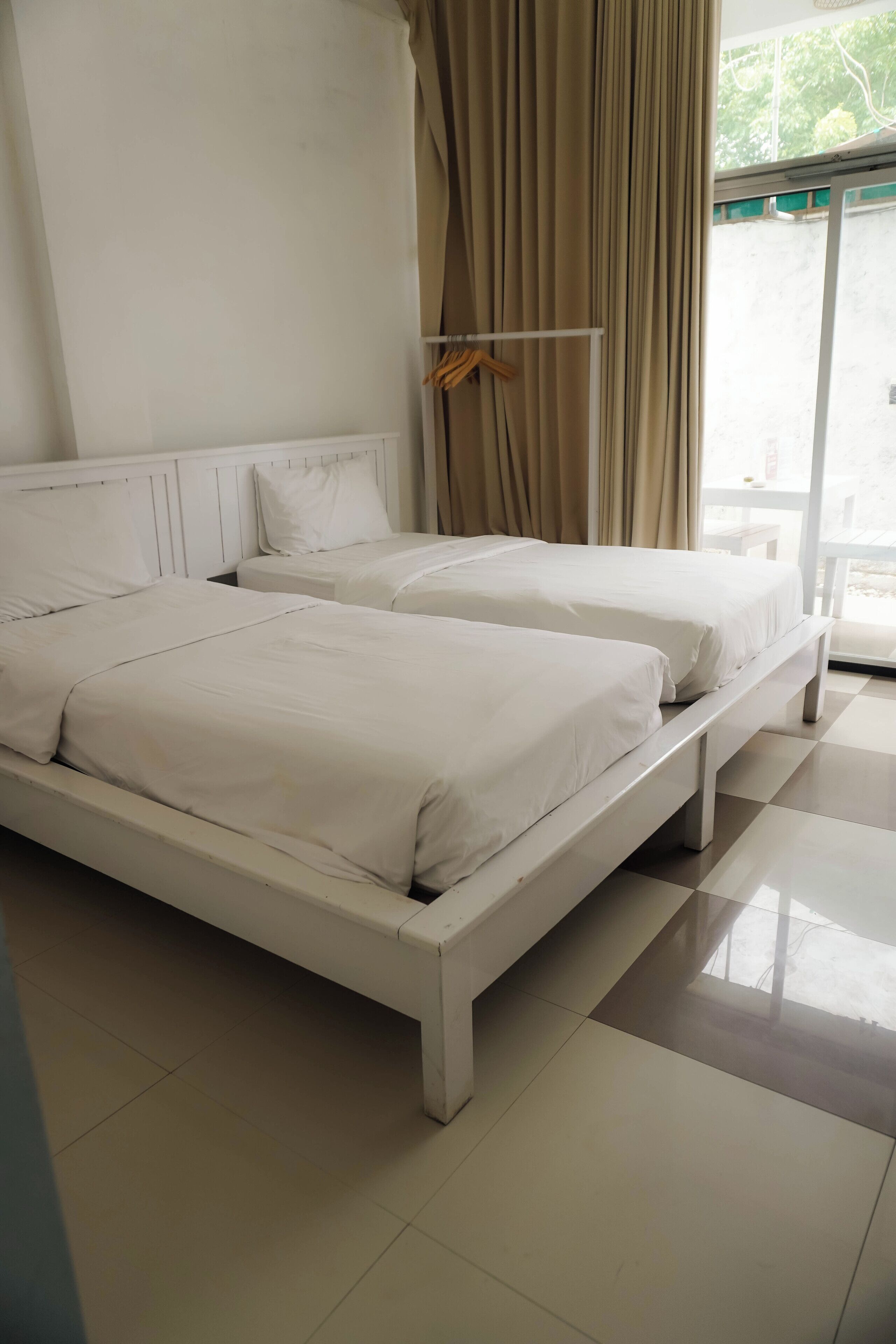 A bedroom with two single beds, a large window with curtains, and a tiled floor.