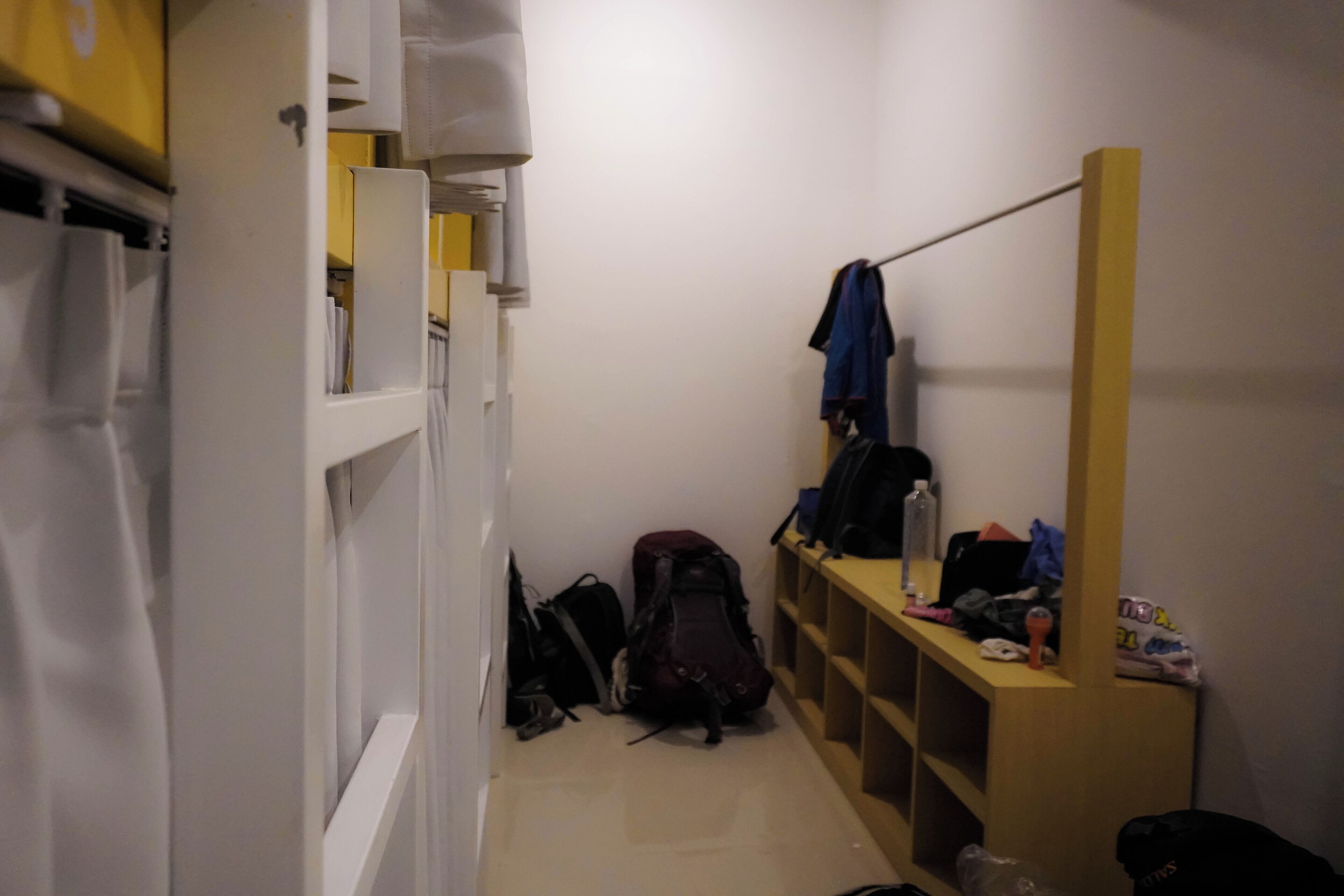 A narrow hallway with a wooden bench, a coat rack, and a shelf with various items.
