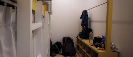 A narrow hallway with a wooden bench, a coat rack, and a shelf with various items.