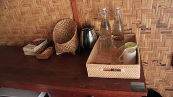 Una mesa de madera con cestas tejidas, una tetera, botellas y una bandeja con una taza y una vela.