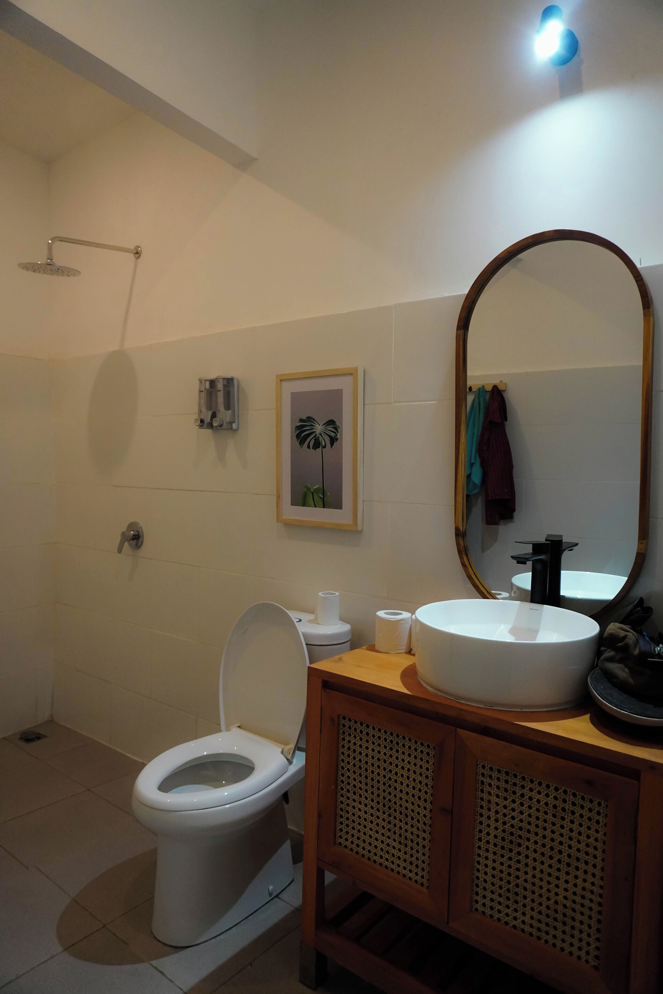 Une salle de bain comprenant des toilettes, un lavabo, un miroir, une douche et un tableau encadré au mur.
