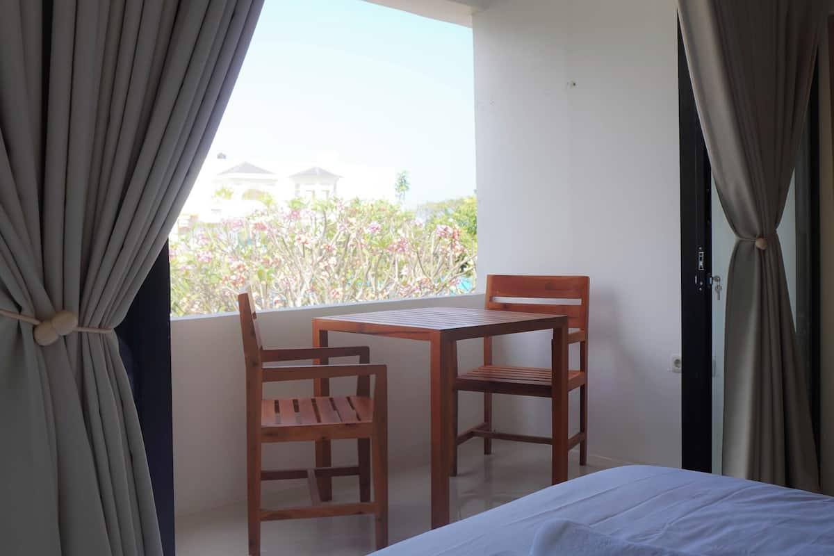 A hotel room with a bed, a table, two chairs, and a balcony with curtains.