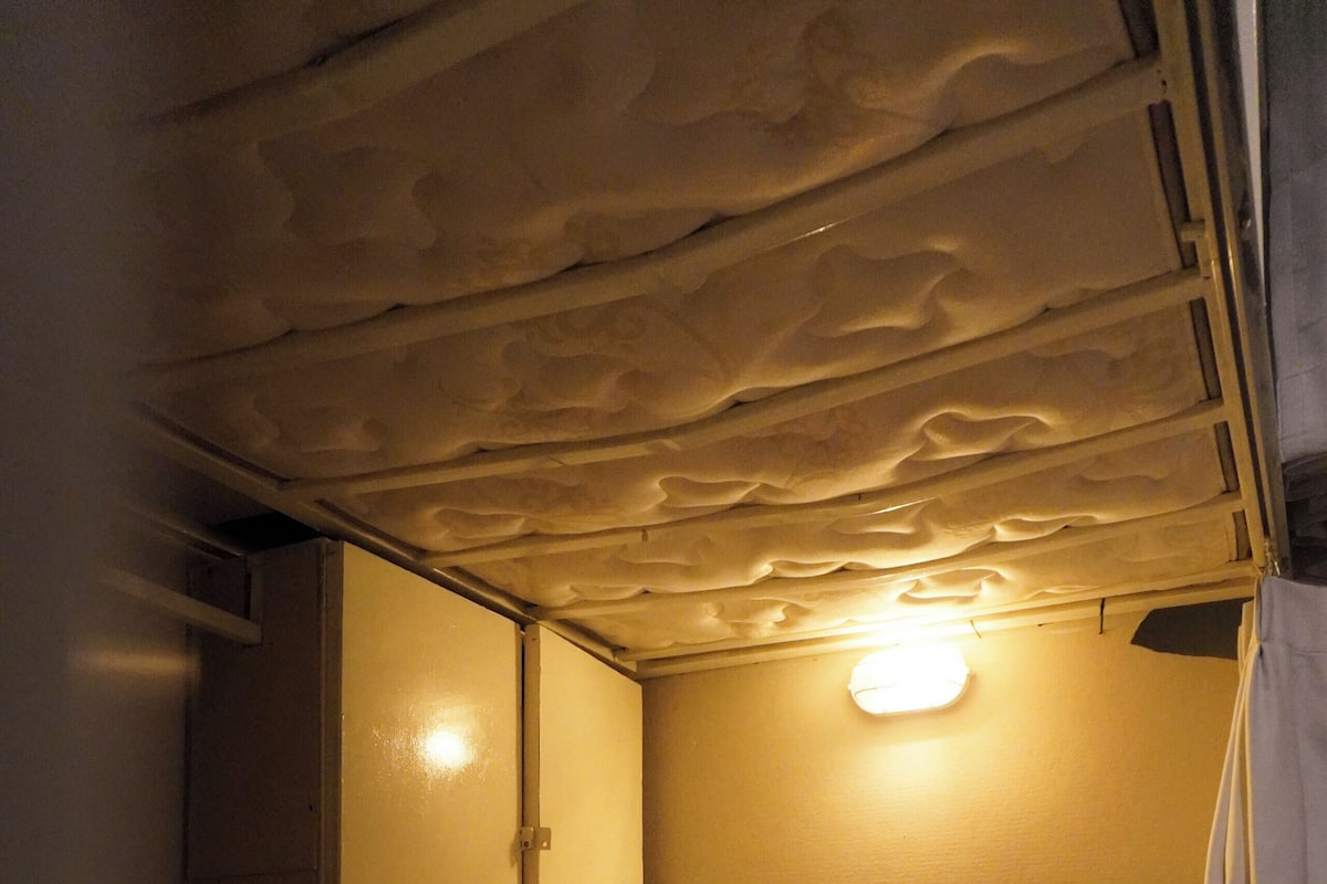 A single bed with a white mattress and pillows, a bedside table, and a wall-mounted light fixture.