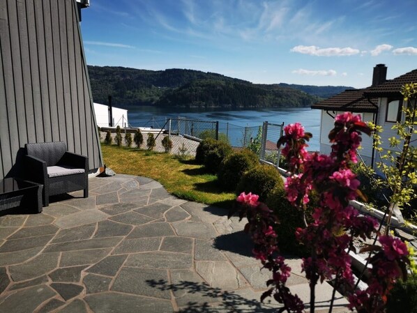 A patio with stone flooring, a wicker chair, and a view of a lake and forested hills. - BJØRNESTRAND FJORDSIDE VIEW (Bergen)