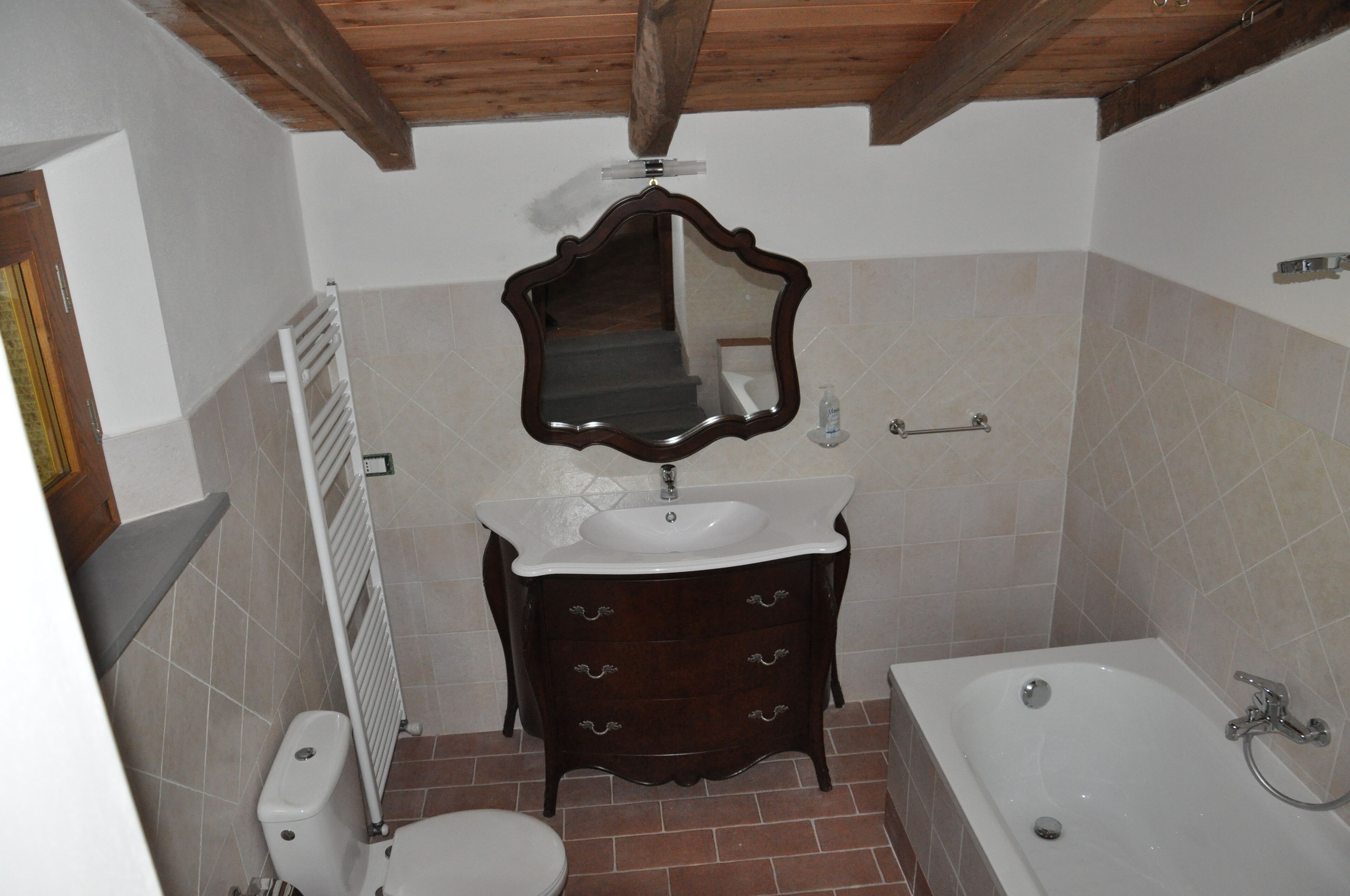 Un baño con techo de madera, un lavamanos blanco, un mueble de tocador de madera oscura, un espejo, una bañera y un inodoro.
